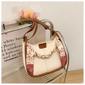 Detail view of cream leather shoulder bag with floral silk scarf and gold chain on stand