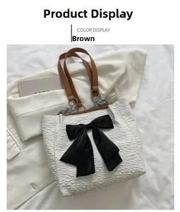 Détail du sac cabas blanc texturé avec un grand nœud noir et une bandoulière en cuir brun