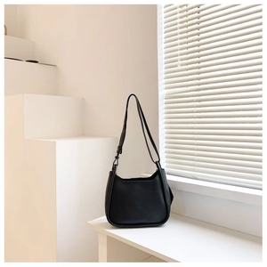 Minimalist black leather underarm bucket bag displayed on a geometric white pedestal
