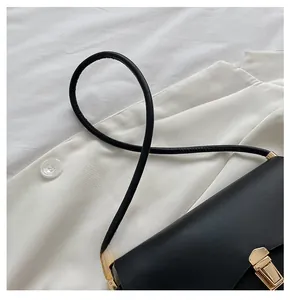 Detail of minimalist black leather saddle bag featuring a sleek gold-tone metal buckle