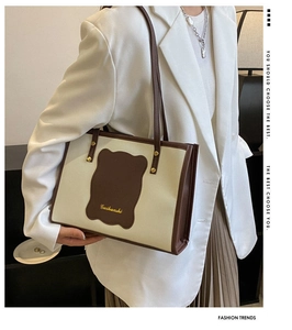 Detail of a contrast color tote bag with brown wave leather patch and gold logo