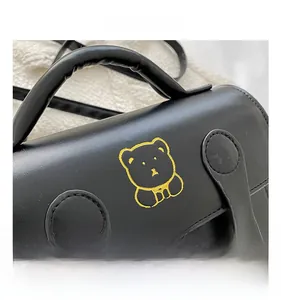 Close-up of black leather handbag with yellow bear embroidery and textured grain