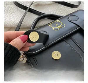 Detail shot of black leather bag featuring gold magnetic clasp and golden bear pattern