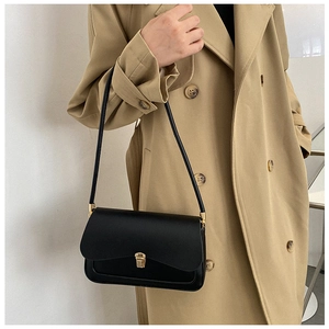 Detailed view of a vintage black leather saddle bag styled with a khaki trench coat