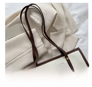 Top view of a minimalist cream tote bag with brown leather trim on a white blazer