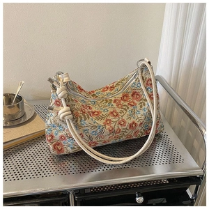 Detail of woven jacquard crescent bag with red floral patterns and knotted rope handle