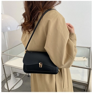 Detail of minimalist black saddle bag with gold buckle worn on a shoulder