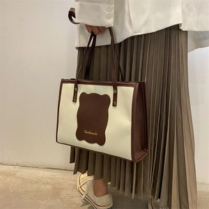 Close-up of minimalist canvas tote bag with brown leather accents and gold logo detail
