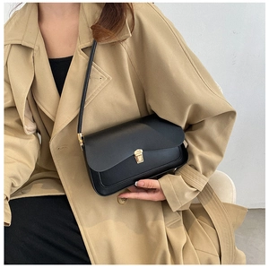 Detail of black leather saddle bag with golden metal buckle clasp on beige trench coat