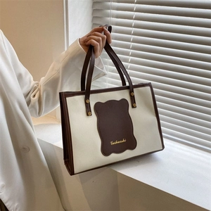 Detail of canvas tote bag with brown leather trim, gold rivets and lettered patch