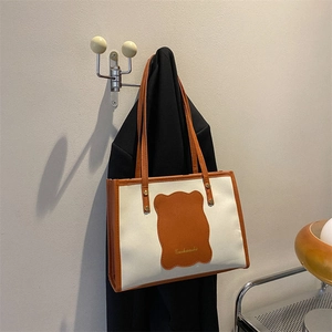 Detail of a color-block tote bag with orange leather trim hanging on a silver wall hook