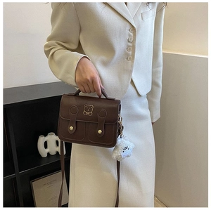 Brown vintage crossbody bag with cute bear print and plush cloud charm on a cream blazer