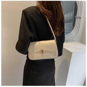 Close-up of minimalist cream leather saddle bag with gold buckle on black blazer