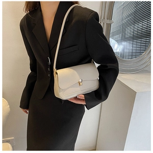 Detail of minimalist cream saddle bag featuring a gold metal clasp and leather strap