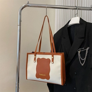 Detail view of canvas tote bag with brown leather trim and shoulder strap on hanger