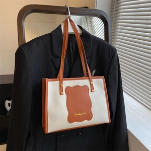 Detail of minimalist cream tote bag with brown contrast trim on a black blazer