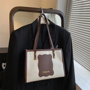 Close-up of minimalist off-white tote bag with contrast brown trim and gold brand logo