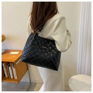 Détail du sac cabas matelassé noir à motif losanges porté par un mannequin en costume