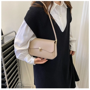 Detail of beige leather saddle bag with gold metal buckle shown on a model