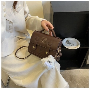 Detail of dark brown retro shoulder bag with embroidered bear and star plush charm