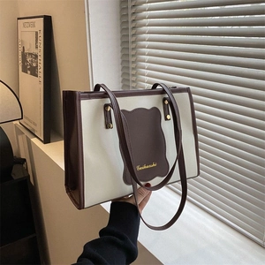 Detailed close-up of large canvas tote bag with brown leather trim and gold lettering