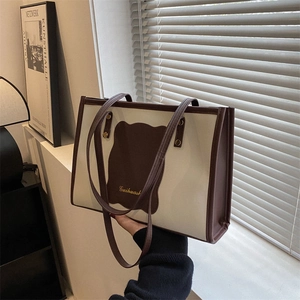 Detail of cream PU tote bag with brown bear patch and gold lettering on shoulder strap