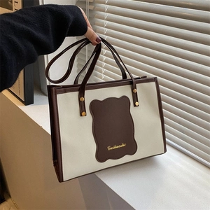 Detail of a minimalist cream and brown tote bag with leather logo patch and thin handles