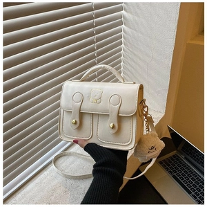 Detail of cream crossbody bag featuring golden bear embroidery and plush charm accessory
