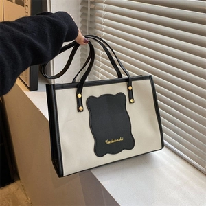 Detail of two-tone canvas tote bag featuring black leather trim and gold brand logo