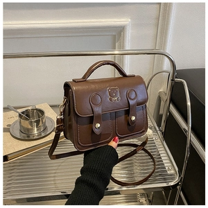 Detail of dark brown vintage handbag featuring a gold bear print and metallic buckles