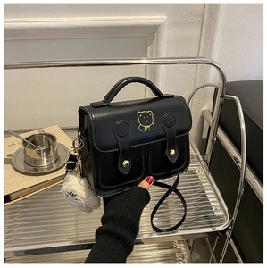 Detail of black crossbody bag with golden bear logo and white plush charm on side