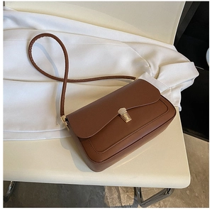 Detail of a brown leather shoulder bag with a vintage gold square buckle on a white chair