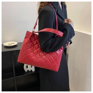 Détail d'un grand sac cabas matelassé rouge brillant porté par un mannequin en veste