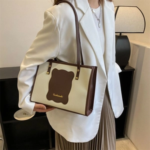 Detail of cream tote bag with brown trim and bear logo patch worn with white outfit