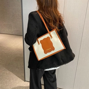 Detail of canvas tote bag with brown leather trim and shoulder straps on a model