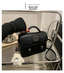 Detail of black crossbody bag featuring gold bear embroidery and white plush charm