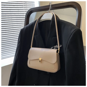 Detail of beige saddle bag with gold metal clasp and chain pin on a blazer