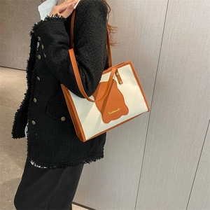 Canvas and orange leather tote bag worn by a model in a stylish minimalist setting