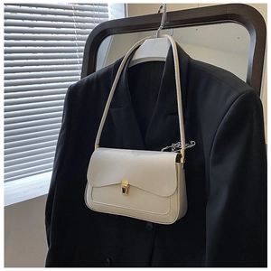 Detail of minimalist cream leather saddle bag with gold metal lock on black blazer