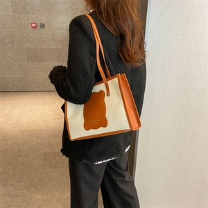 Chic cream canvas tote bag with orange leather trim and bear patch shown on shoulder