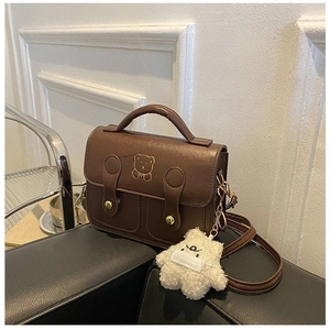 Detail of brown vintage crossbody bag with gold bear motif and plush charm accessory
