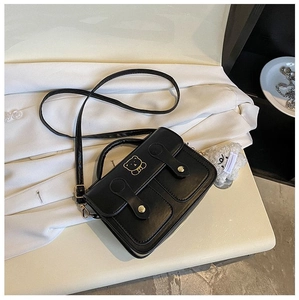 Detail of black leather square bag with gold bear buckle on a white blazer background