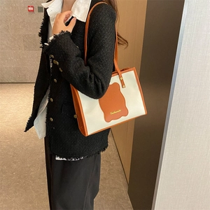 Close-up of off-white canvas tote with orange leather trim and brand logo patch