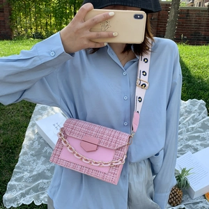 Pink tweed crossbody bag with floral wide strap and decorative chain shown outdoors