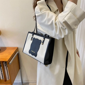 Detail view of contrast tote bag with wavy patch and brand lettering on shoulder
