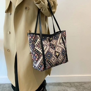 Ethnic style geometric woven tote bag with leather straps on a khaki trench coat model