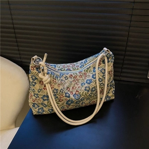 Retro ethnic floral jacquard underarm bag with cream rope straps on a dark surface