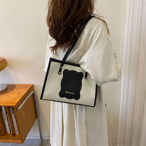 Detail of minimalist cream leather tote bag with black contrast trim and gold logo