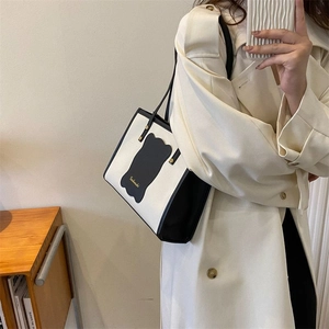 Detail of a black and white canvas tote bag with leather trim on a beige trench coat