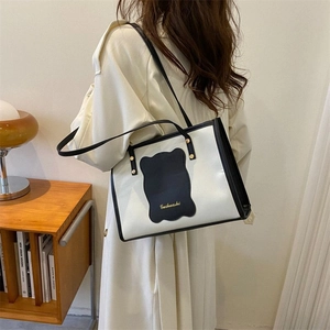Detailed shoulder view of a cream tote bag with black piping and gold logo details